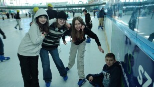 grupa dzieci na łyżwach w tym jeden chlopiec siedzi na lodowisku