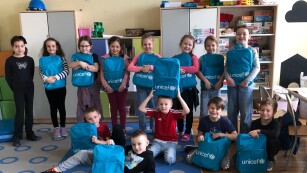grupa kilkunastu uśmiechniętych dzieci z niebieskimi plecakami z logo UNICEF