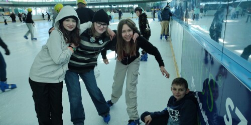 grupa dzieci na łyżwach w tym jeden chlopiec siedzi na lodowisku