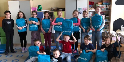 grupa kilkunastu uśmiechniętych dzieci z niebieskimi plecakami z logo UNICEF